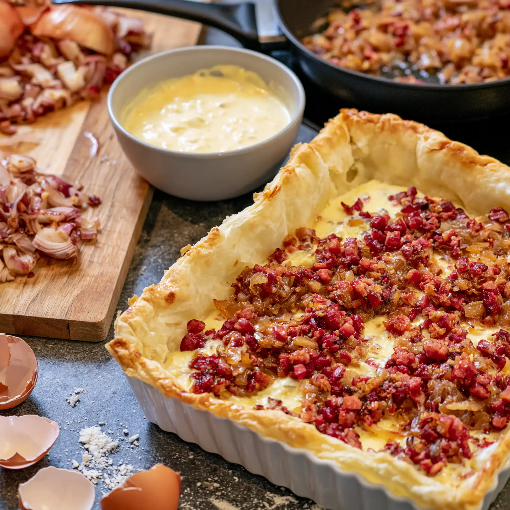 Vorbereitung von Zwiebelkuchen mit gedünsteten Zwiebeln, Speck und Blätterteig in einer Backform